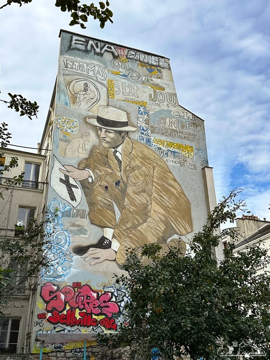 : Fresque murale à Belleville : un homme en costume beige et chapeau tient une pancarte, entouré de réclames anciennes.