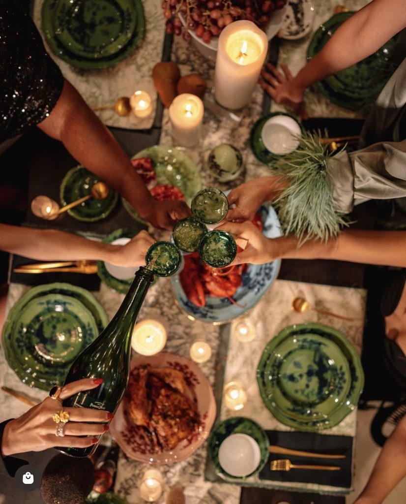 Table dressée à la bougie, vaisselle verte et bleue, verres qui trinquent au-dessus de crustacés et d'un poulet rôti
